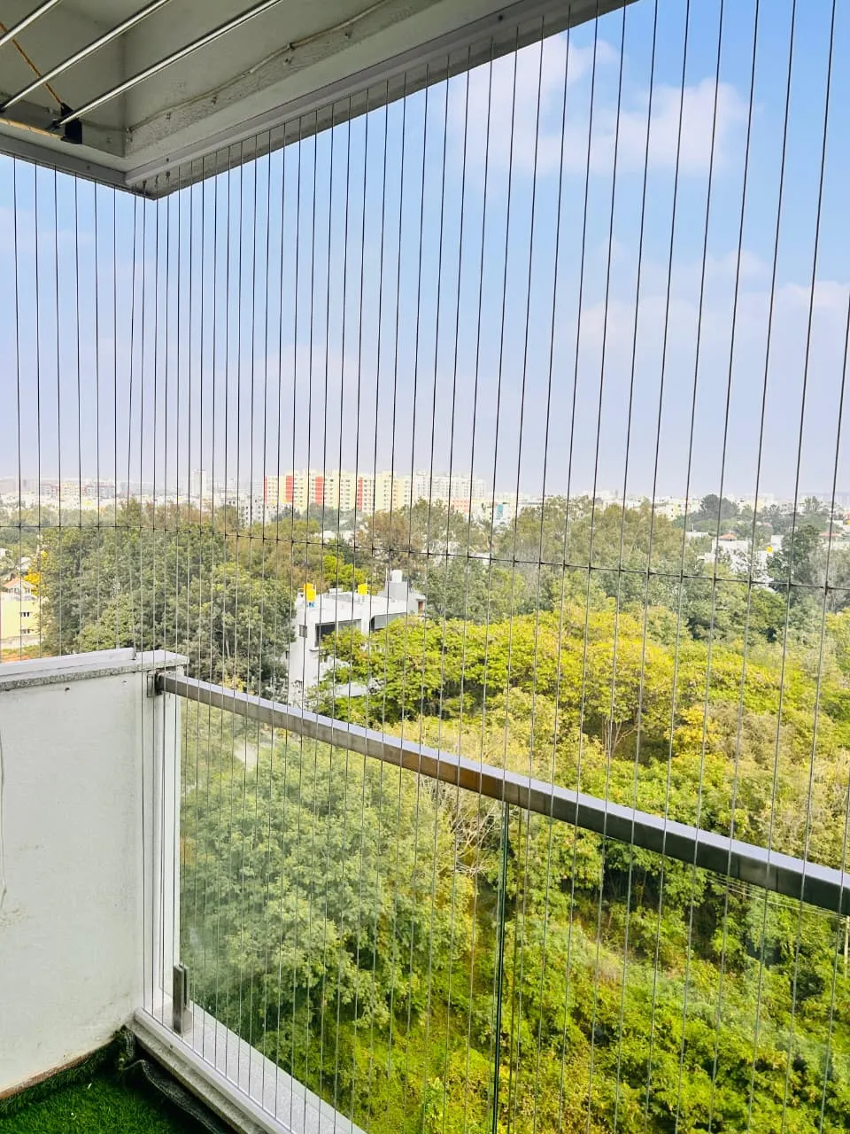 Invisible grill fitted over a glass-railing balcony with treetop views