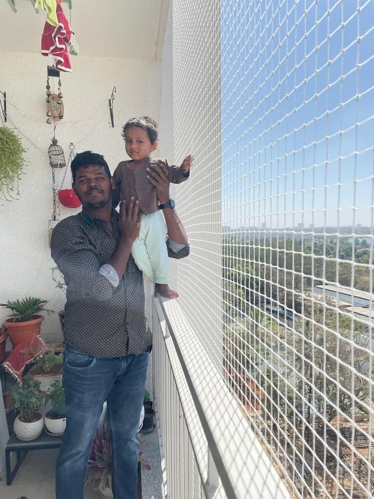 Father holding a toddler beside a high-rise balcony safety net with lake view