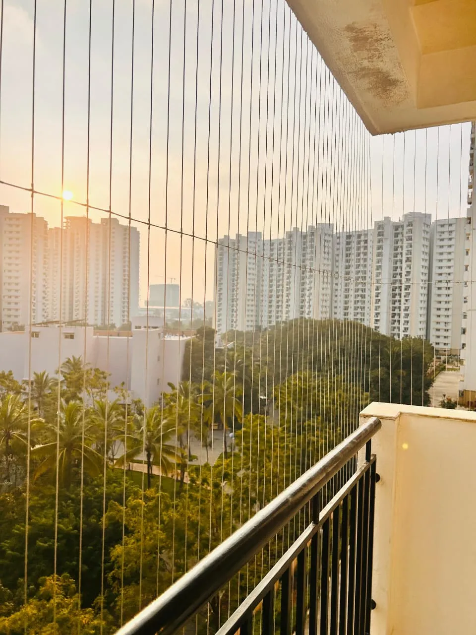 Invisible grill on a high-floor balcony at sunset overlooking apartment towers