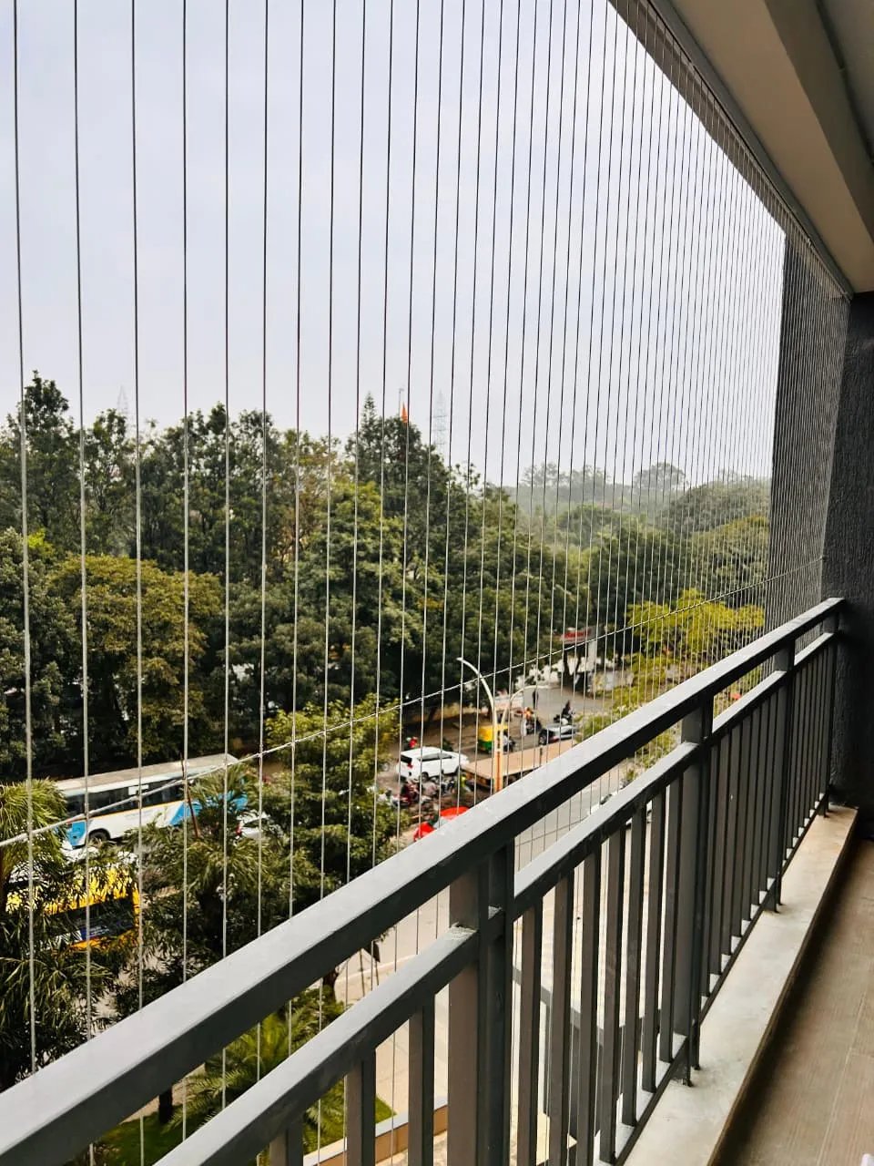 Invisible grill cables along a long apartment balcony facing a tree-lined road