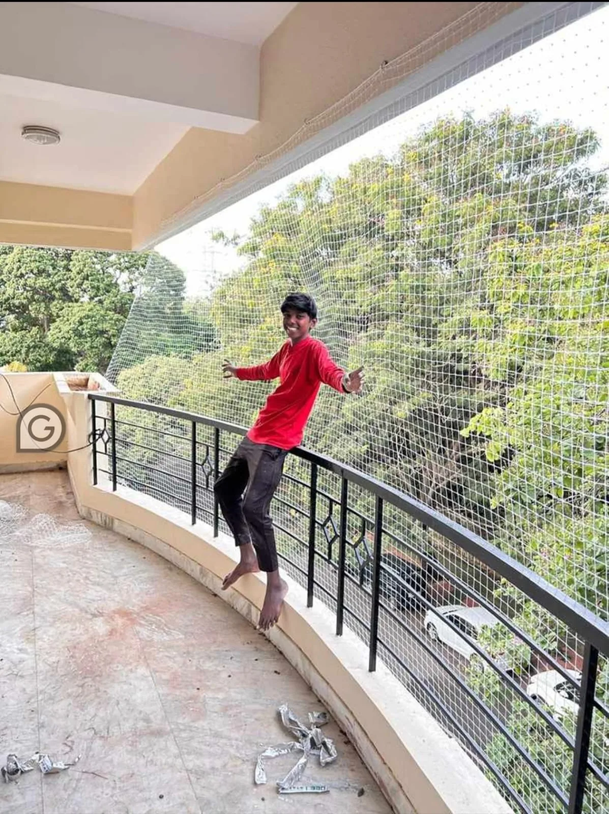 Boy leaning on a balcony railing protected by a children safety net overlooking greenery