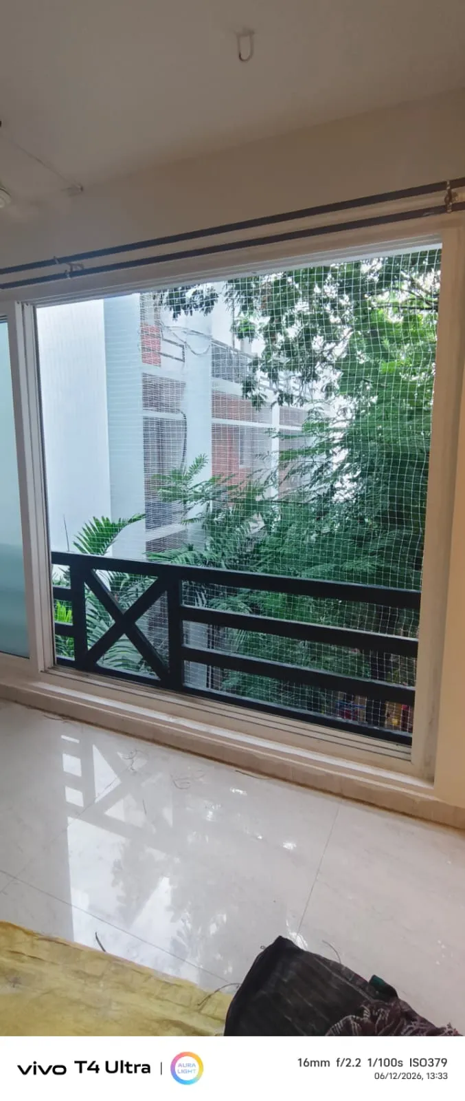 Bird net fitted over a living room window opening onto a tree-lined balcony