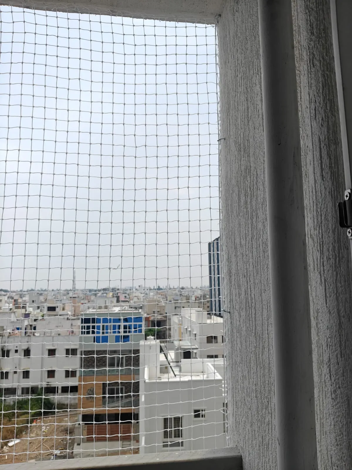 Close-up of a pigeon net fitted to a utility opening with city view behind